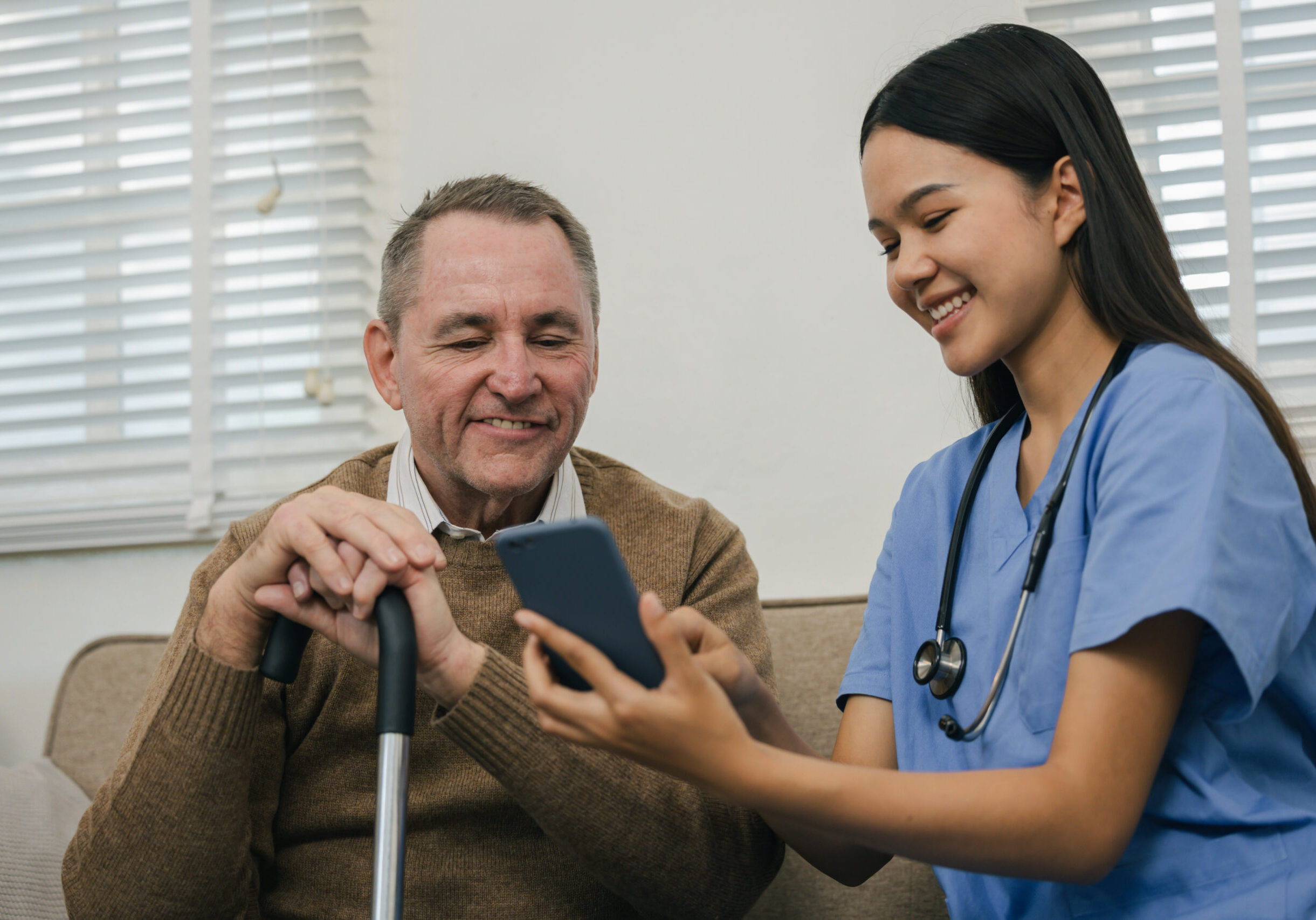 Happy nurse helps senior man with a smartphone at clinic, healthcare support for the elderly.